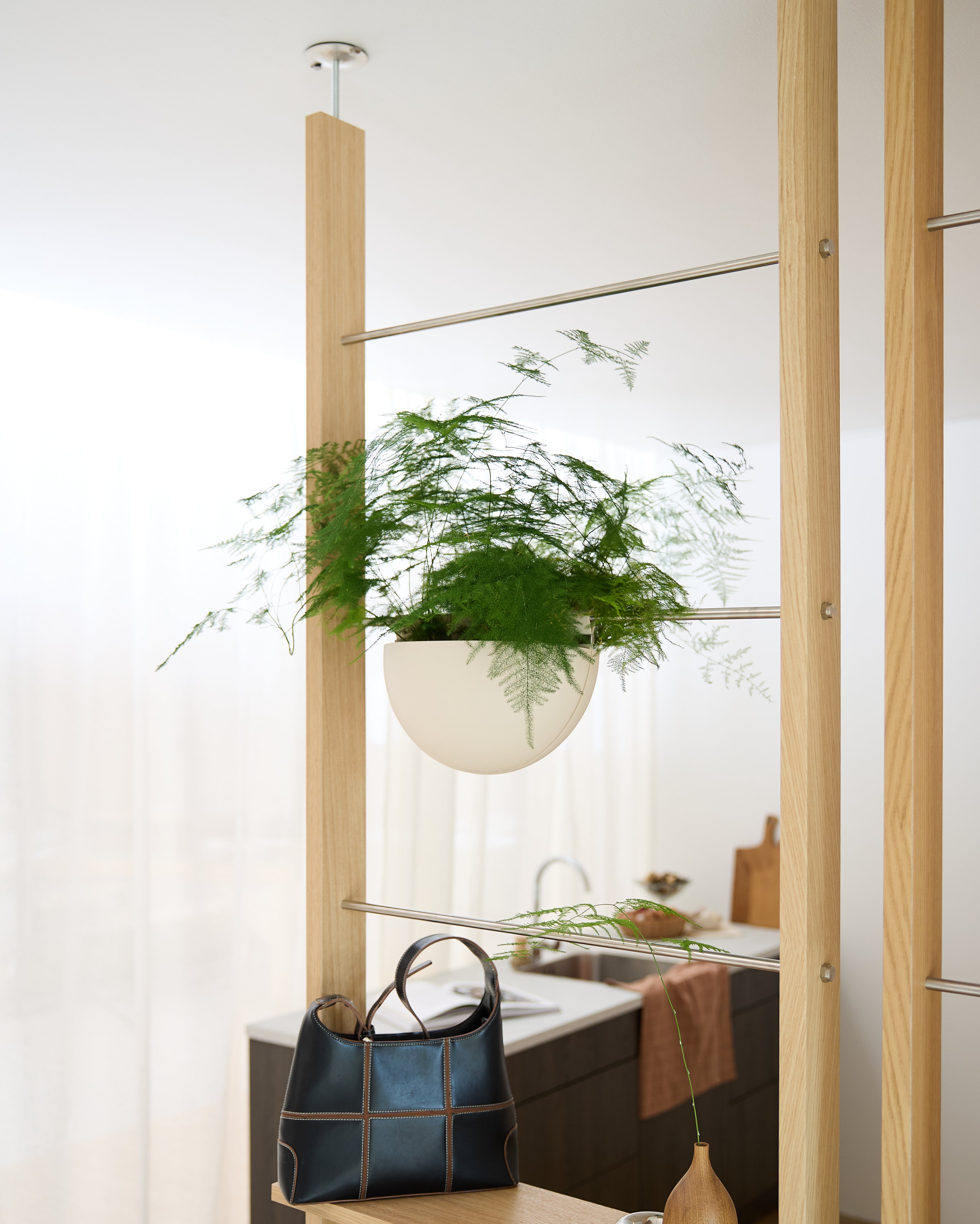 A Gro Soft Pocket (4L) by WoodUpp is mounted on a wooden frame above a black handbag in a bright, modern kitchen.